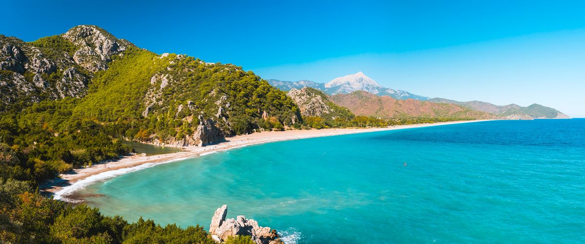 Panoramatický pohled na pláž Çıralı s modrým Středozemním mořem obklopenou zelenými horami v turecké provincii Antalya.