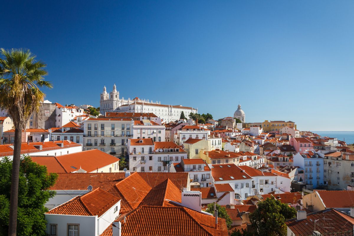 Historická čtvrť Alfama v Lisabonu s typickými bílými domy a červenými střechami na pozadí baziliky sv. Vincenta a národního panteonu.
